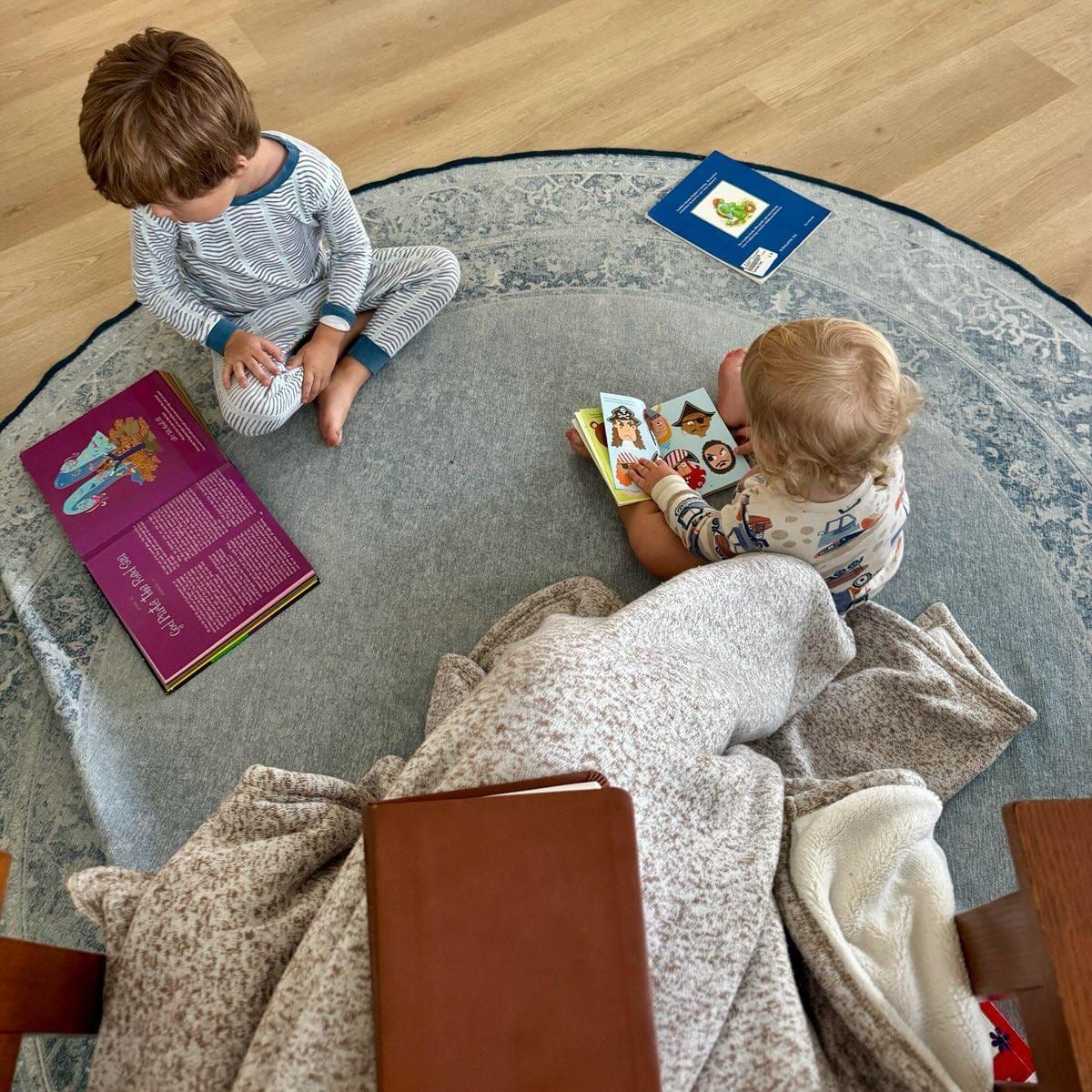 Two little ones reading picture books on a rug